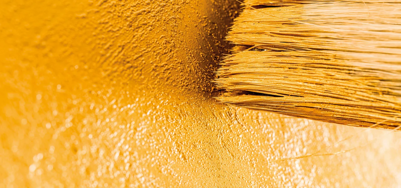 Nahaufnahme, Pinsel der eine goldene Wandfarbe aufträgt 