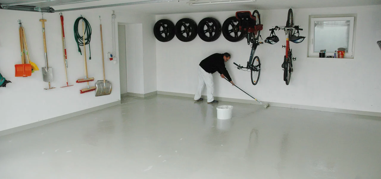 Malermeister, der eine Bodenbeschichtung in einer Garage aufträgt