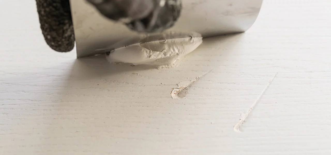 Spachtelmasse wird mit einer Spachtel über Holzmacken gezogen