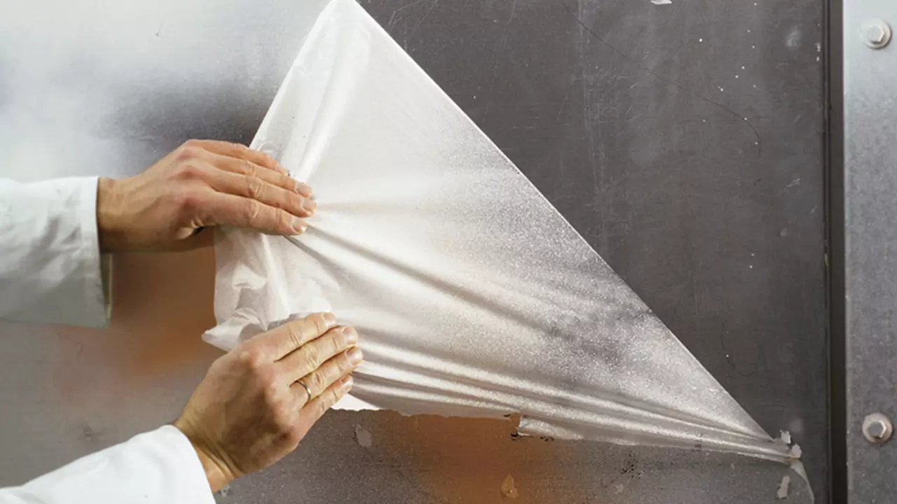 Person zieht den getrockneten Abziehlack von einer metallischen Oberfläche.